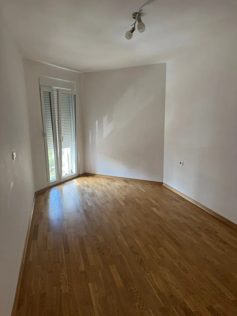 Prazna soba sa parketom i vratima za izlaz na terasu.