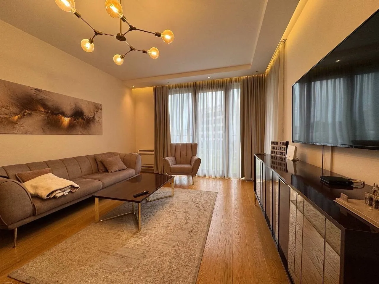 A modernly furnished living room with a comfortable sofa, TV, and warm lighting.