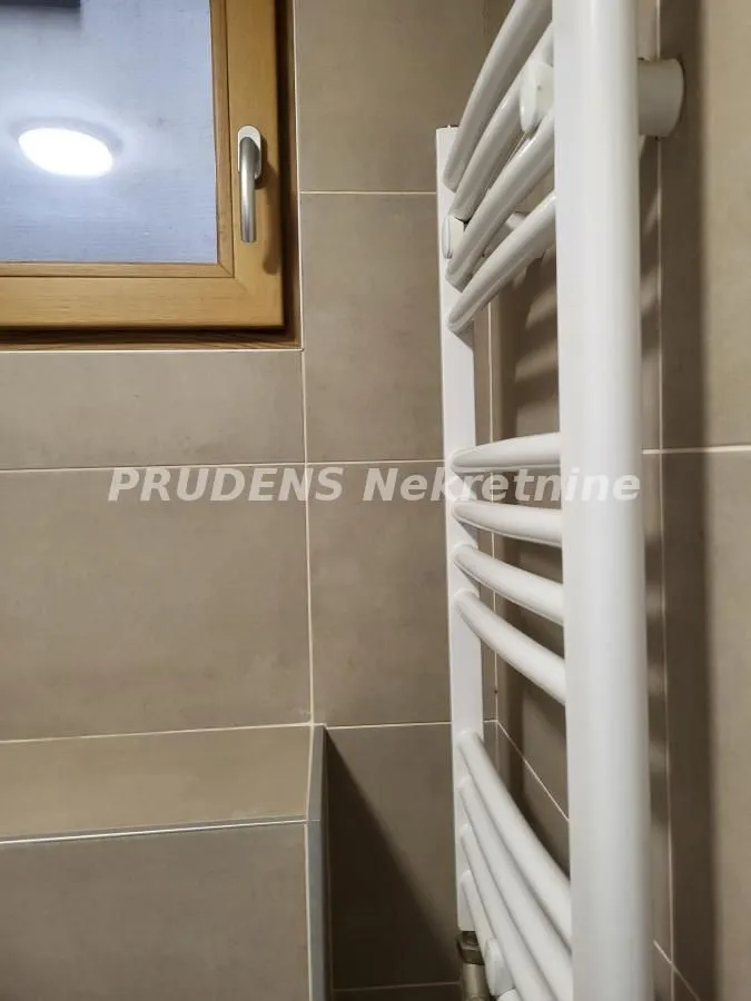 Pogled na beli radijator i keramičke pločice u kupatilu.