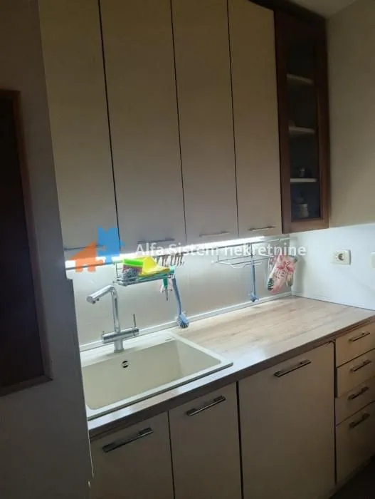 Deo kuhinje sa sudoperom, radnom pločom i gornjim elementima.