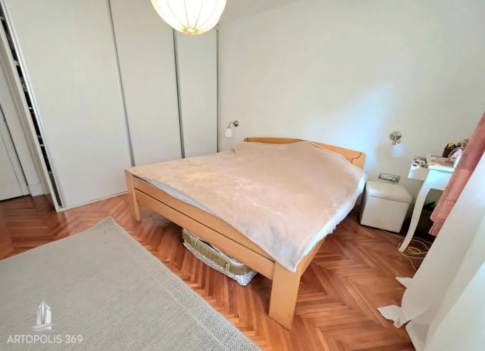 Spavaća soba sa bračnim krevetom, drvenim podom i ugradnim plakarom.