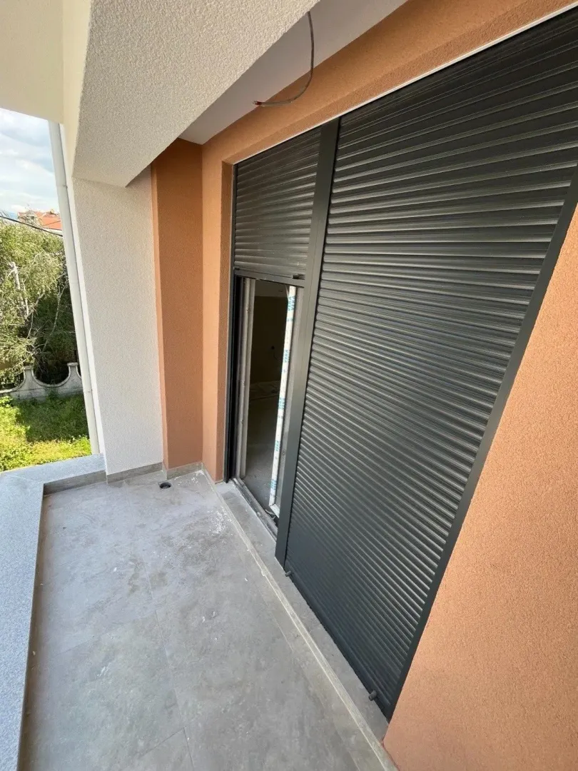 Nenamješten balkon sa spuštenim roletnama i pogledom na dvorište.