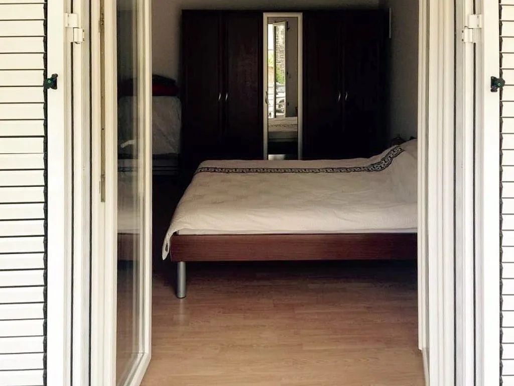 Pogled izvana kroz otvorena balkonska vrata na namještenu spavaću sobu sa bračnim krevetom i ormarom.