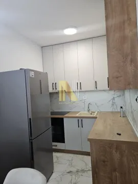 Manja opremljena kuhinja sa belim elementima, drvenim radnim površinama i frižiderom. - image 7