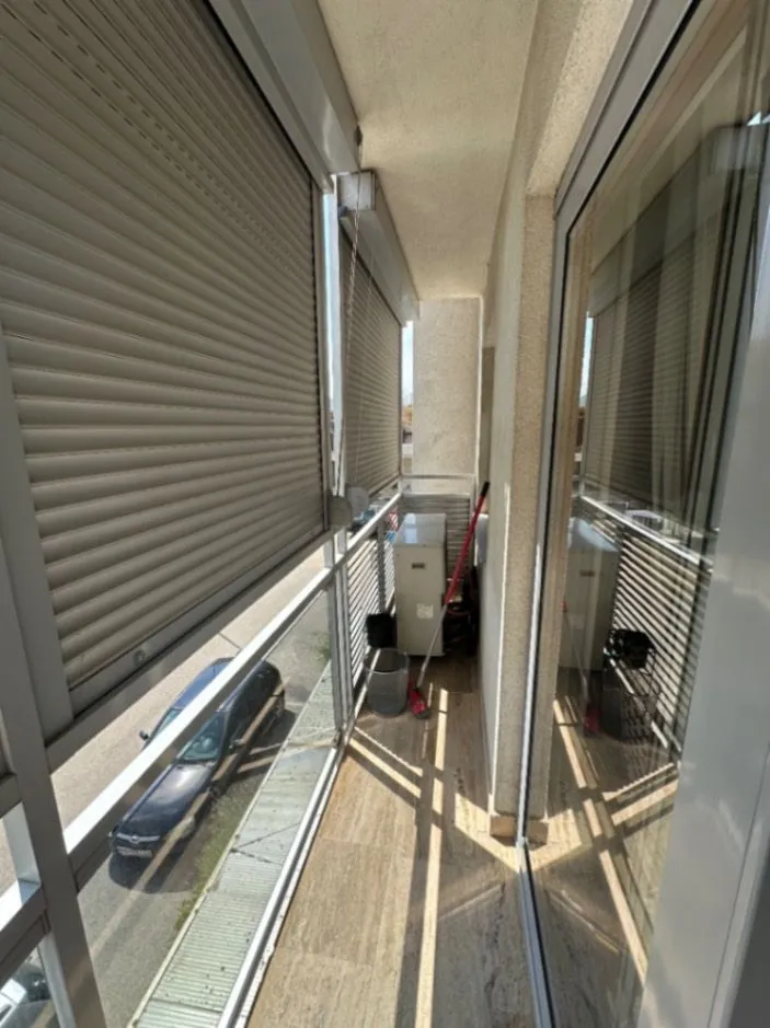 Narrow balcony with lowered roller blinds and street view.