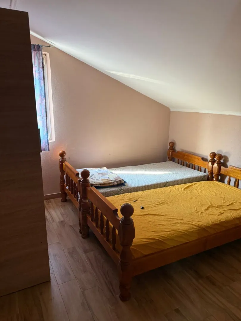 Attic bedroom furnished with wooden beds with mattresses and a small window.