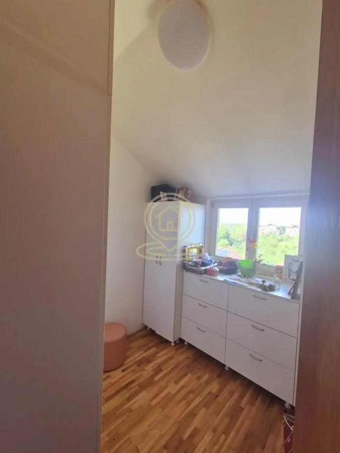 Manja soba sa drvenim podom, belom komodom i prozorom.