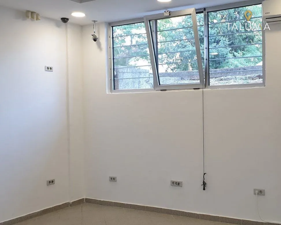 Empty room with white walls, tiled floor, and a window with security bars.