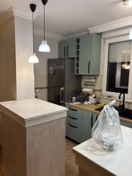 Kuhinja sa svijetlozelenim kabinetima, frižiderom i kuhinjskim ostrvom u prvom planu. - image 3