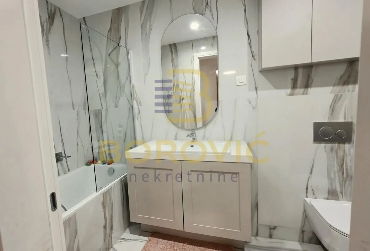 Modern bathroom with a washbasin, shower cabin, and marble tiles.