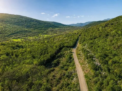 Pogled iz vazduha na zelenu dolinu i seoski put okružen brdima. - image 5