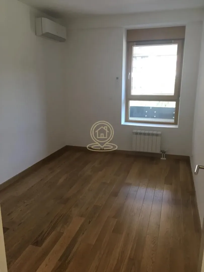 Empty room with wooden flooring, air conditioning unit, and a window.