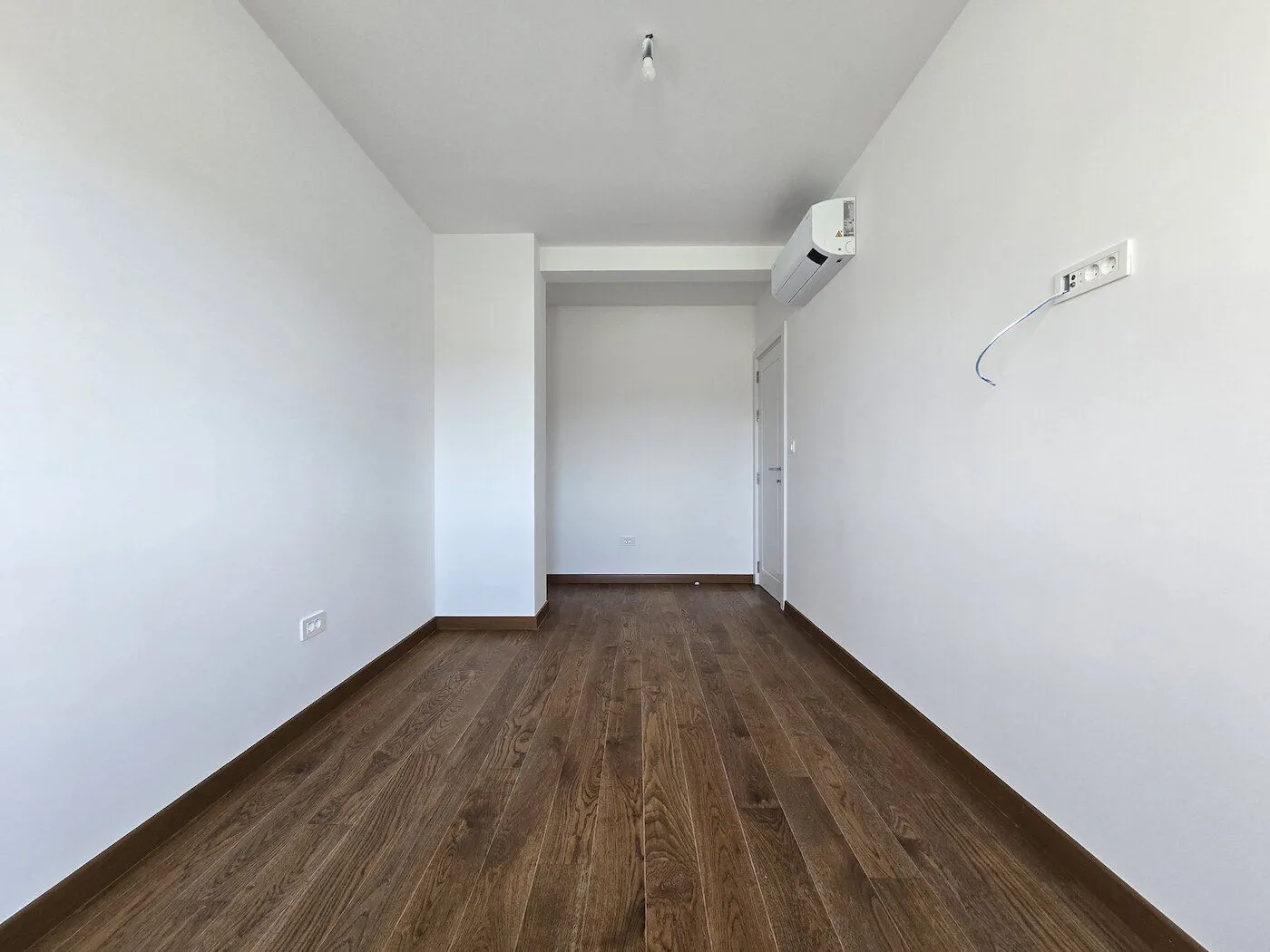 Empty room with white walls and dark wooden floor.