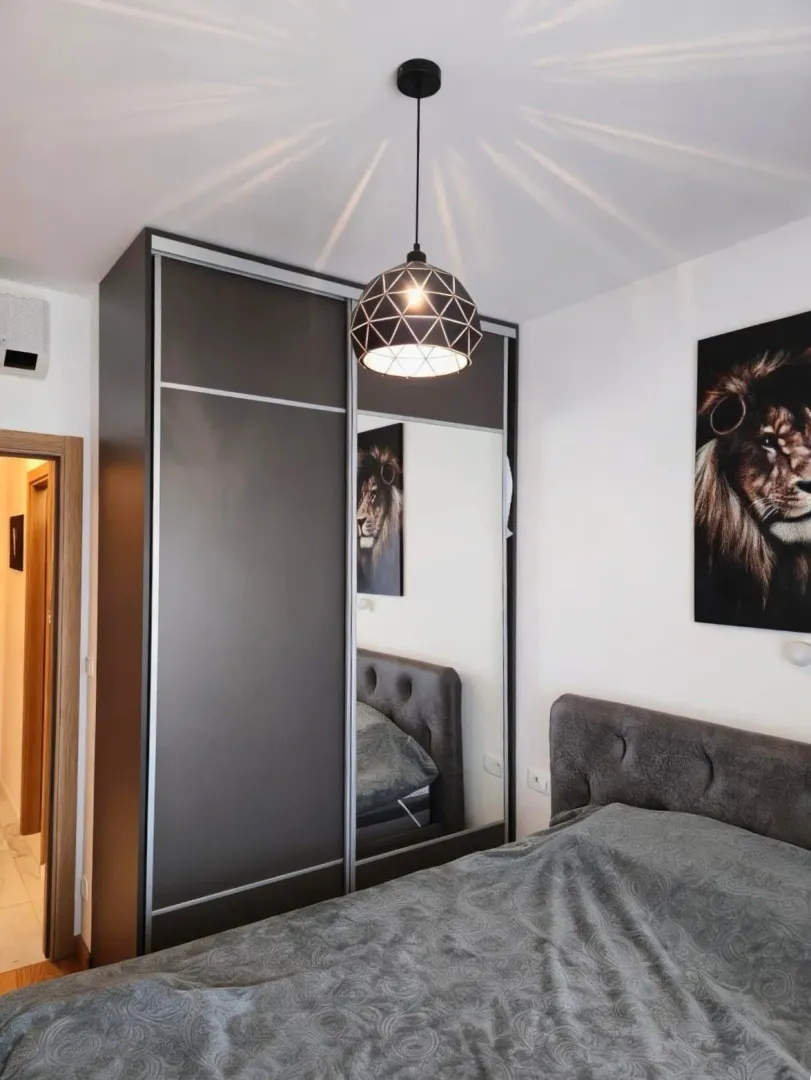 Namještena spavaća soba sa bračnim krevetom, velikim garderoberom i modernim lusterom.