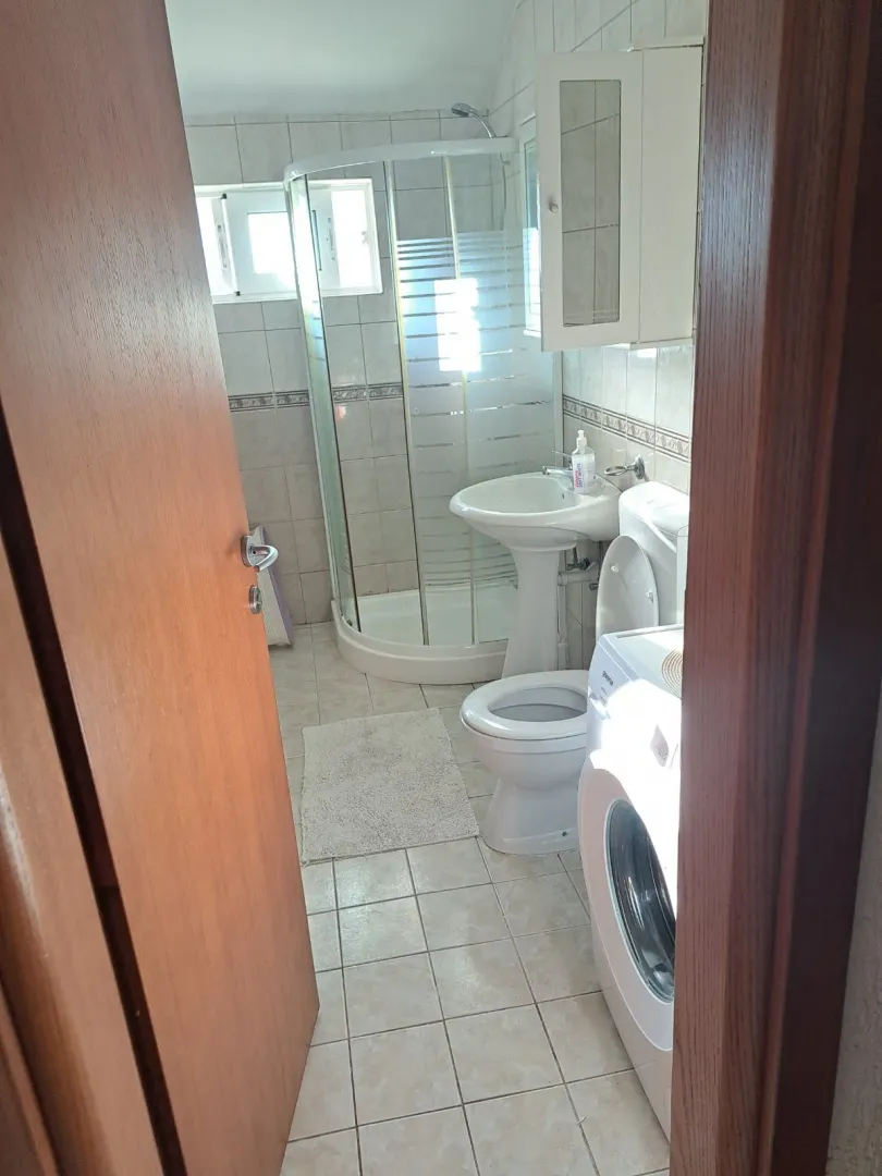 Pogled na kupatilo sa tuš kabinom, umivaonikom, WC šoljom i mašinom za veš.