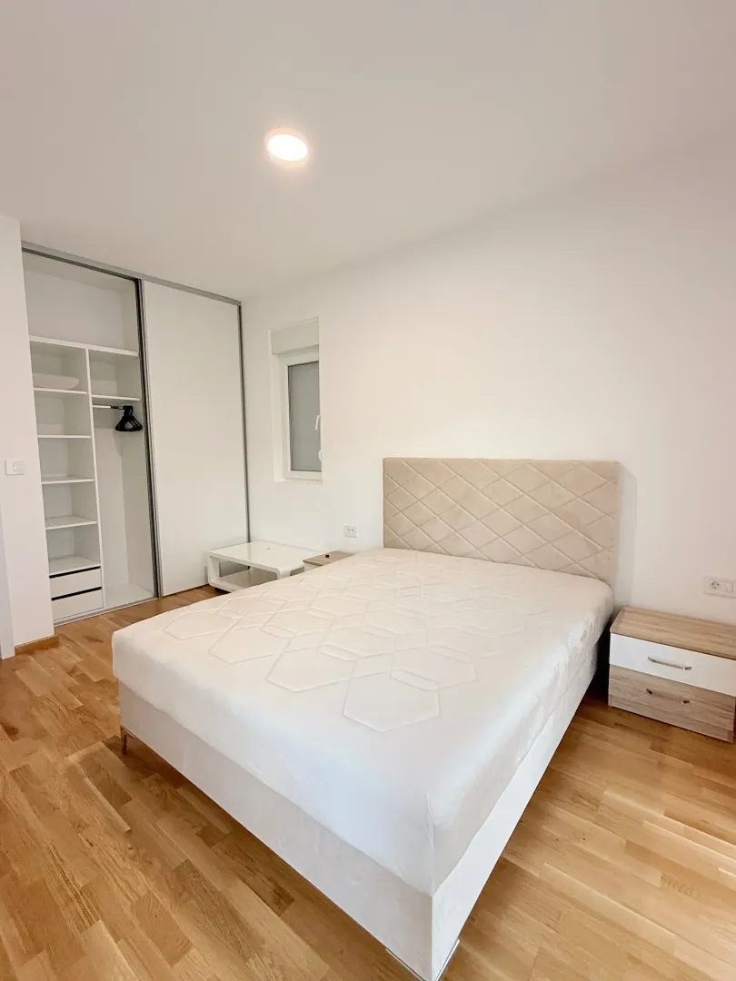 Svijetla spavaća soba sa bračnim krevetom, plakarom i noćnim stočićima.