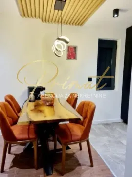 Trpezarija sa drvenim stolom i narandžastim stolicama ispod moderne plafonske rasvete. - image 11