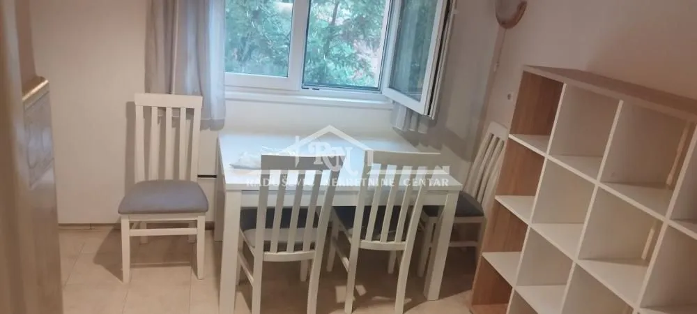 Dining area with a white table, chairs, and a shelving unit by the window.