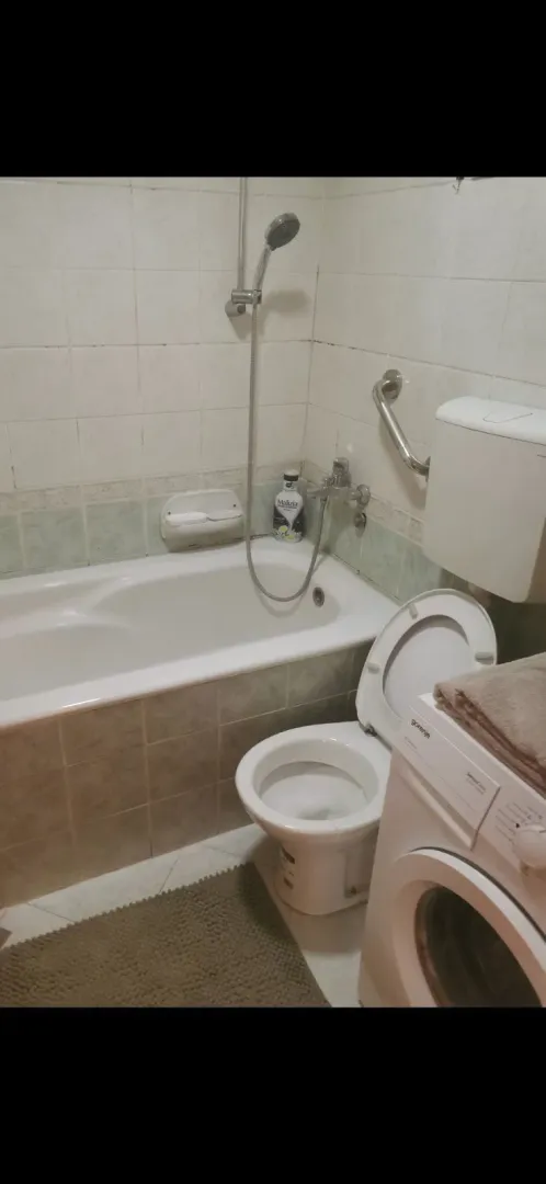 A simple bathroom featuring a bathtub, toilet, and washing machine.