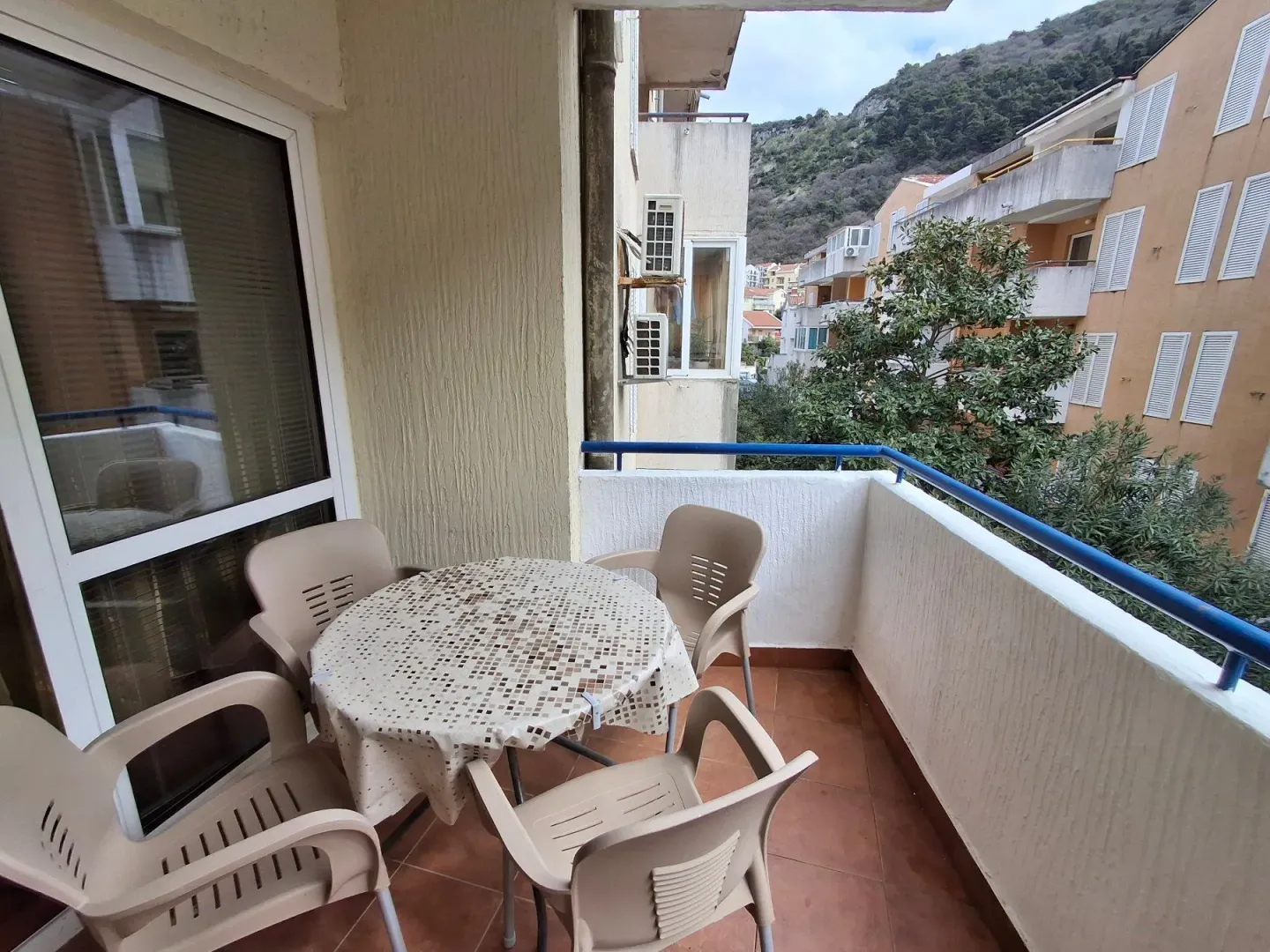 Natkriveni balkon sa garniturom za sjedenje i pogledom na naselje i okolna brda.