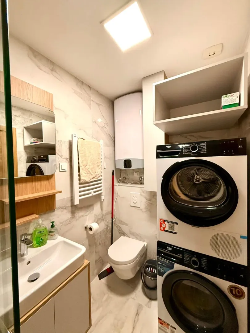 Moderne kupatilo sa umivaonikom, WC šoljom, tuš kabinom i ugrađenom mašinom za veš.