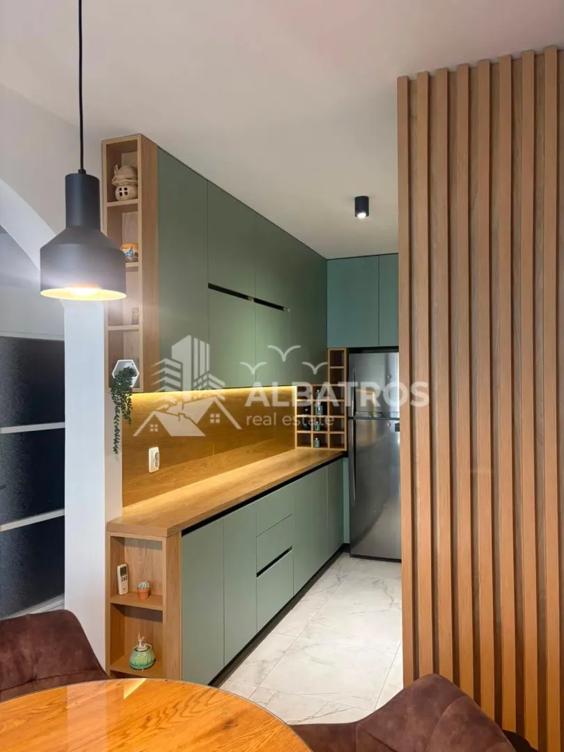 Modern kitchen with green cabinets, wooden details, and a built-in refrigerator.