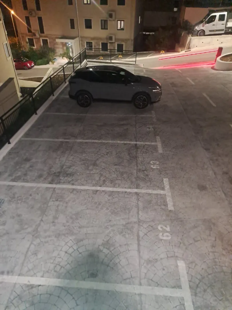 Pogled na parking prostor ispred stambene zgrade noću.