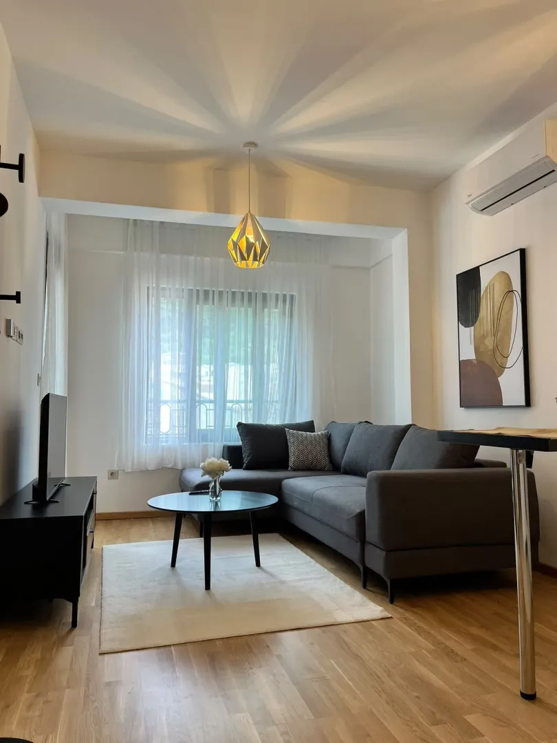 Moderna i uredna dnevna soba sa ugaonom garniturom i TV-om.
