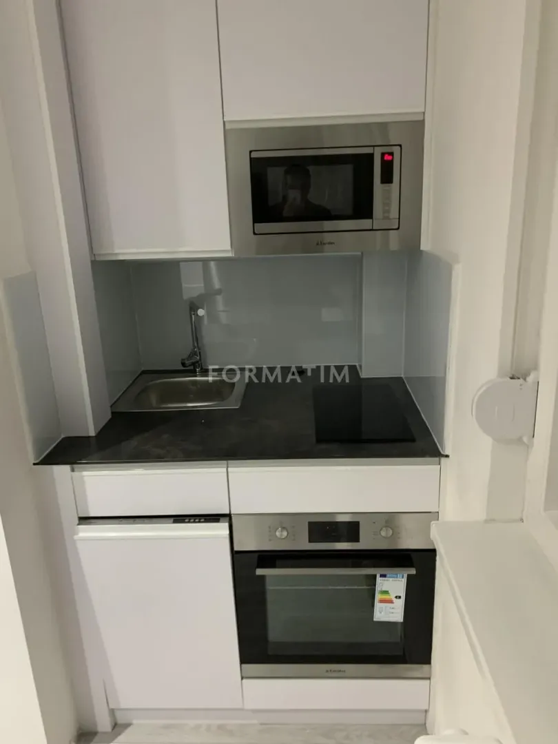 Manja bela kuhinja sa ugradnom rernom, ploçom, sudoperom i mikrotalasnom pećnicom.