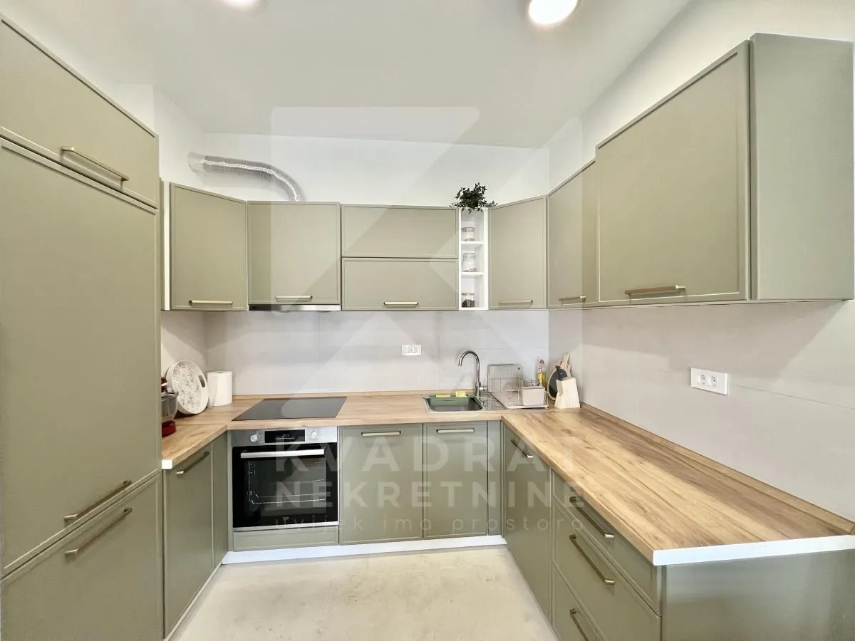 Modern U-shaped kitchen with green cabinets and wooden countertop.