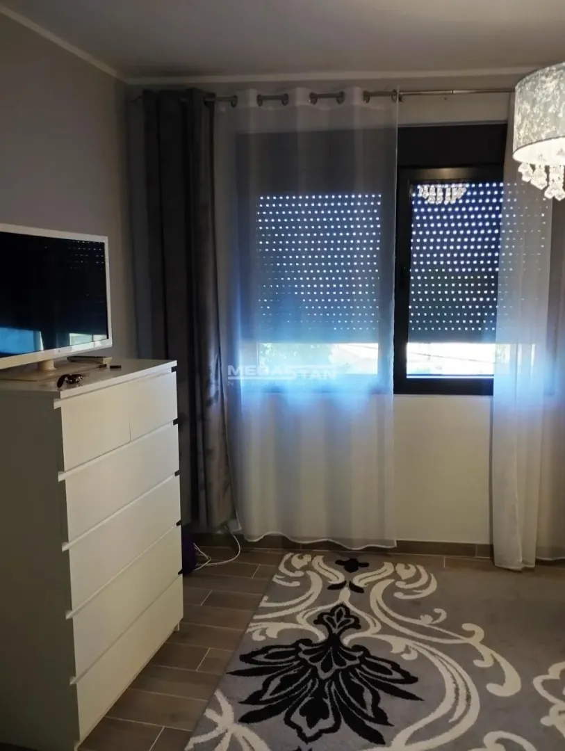 Spavaća soba sa belom komodom, televizorom i prozorom sa zavesama.