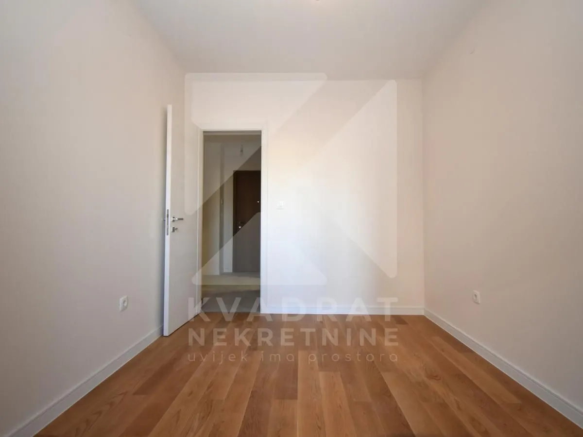 Prazna soba sa drvenim podom i otvorenim vratima.