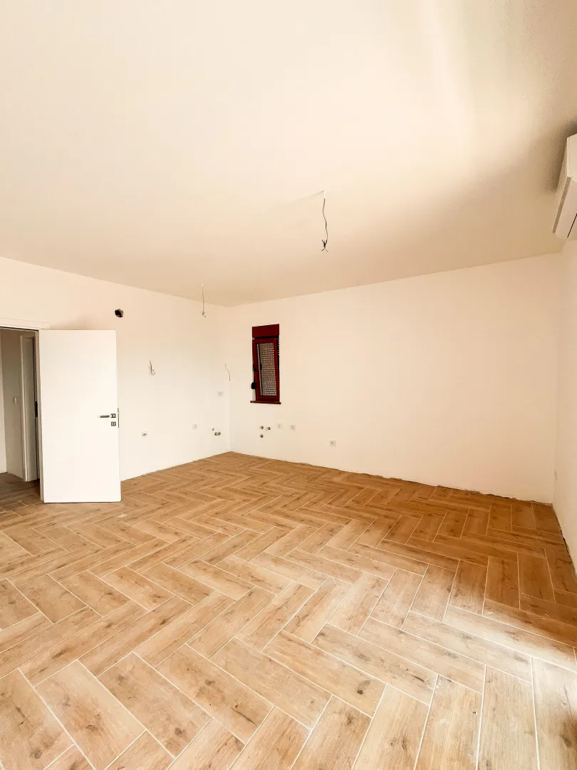 Prazna prostorija sa drvenim podom i bijelim zidovima.