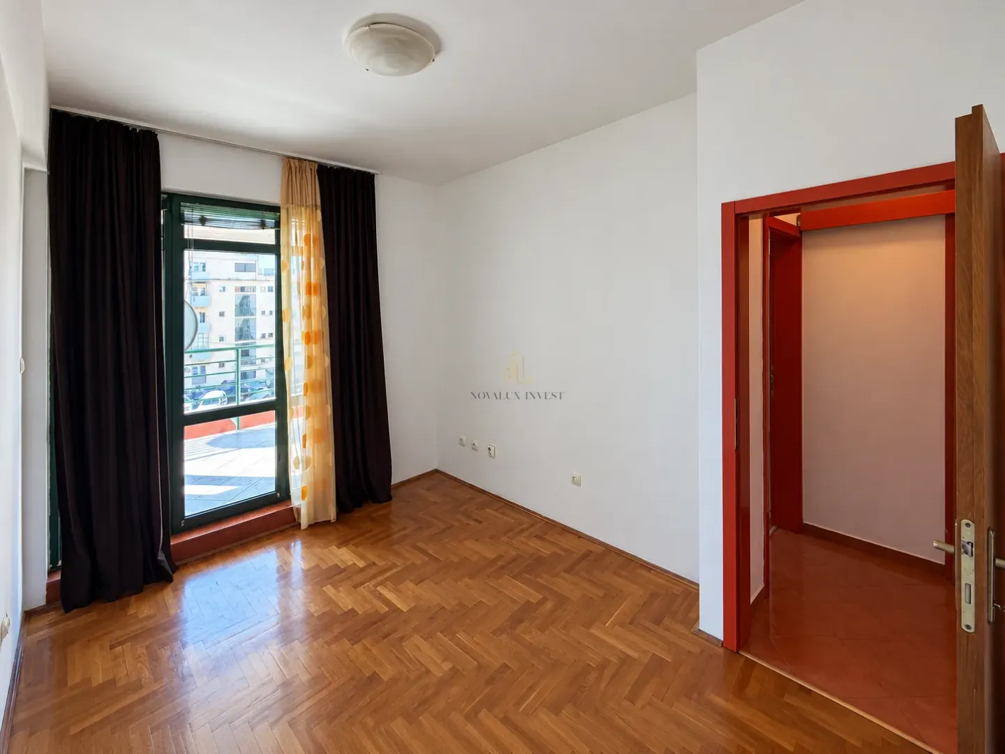 Empty room with parquet flooring, a window, and a door leading to the hallway.