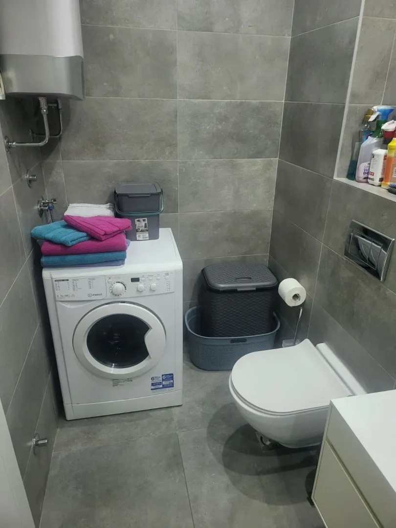 A bathroom featuring a washing machine, toilet, and grey wall tiles.