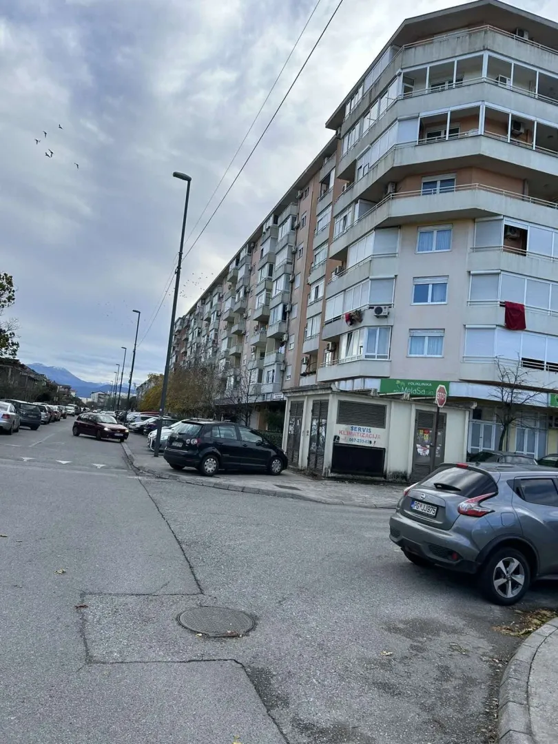 Višespratna stambena zgrada pored ulice sa parkiranim automobilima.