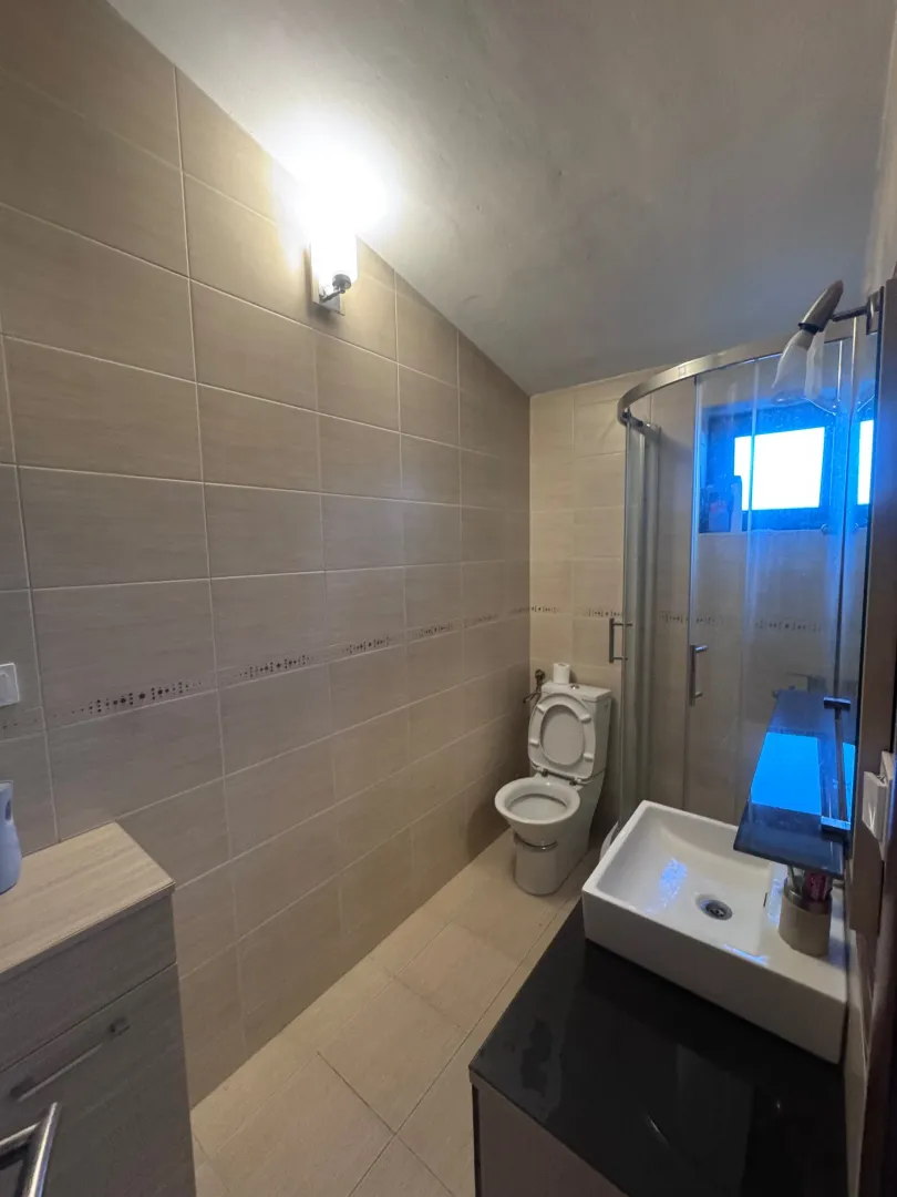 Compact bathroom with a shower cabin, washbasin, and toilet in beige tones.