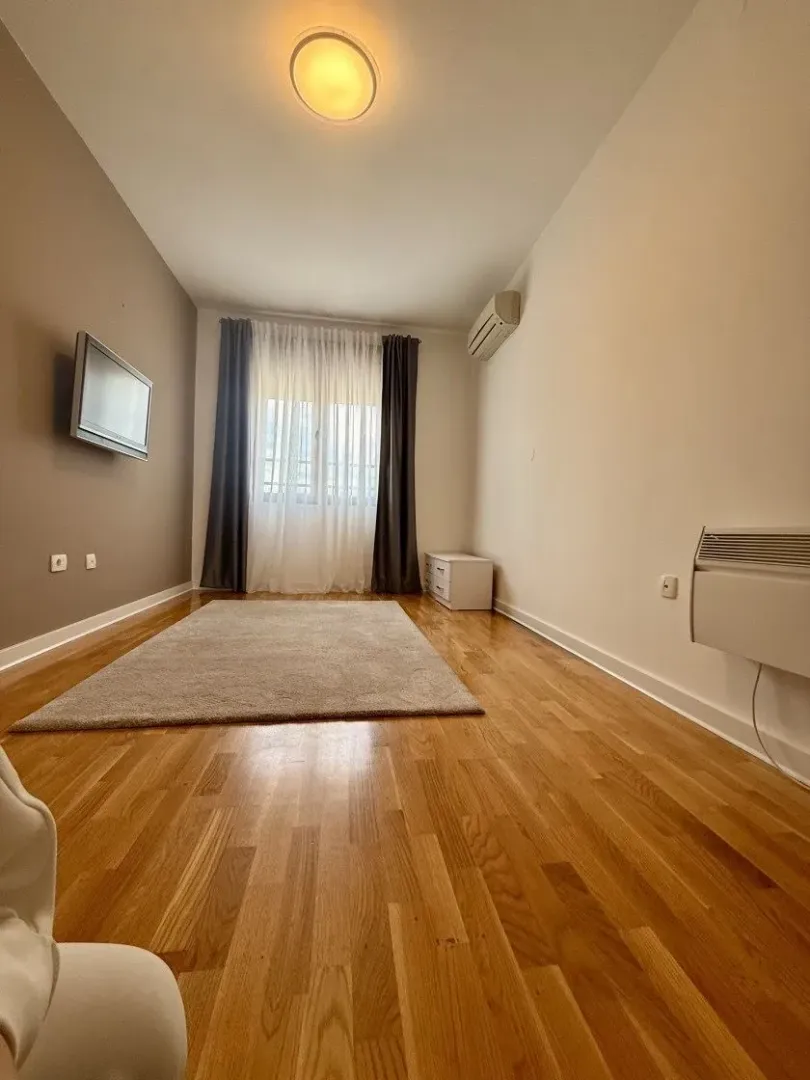 Empty living room with wooden flooring, a rug, and a window.