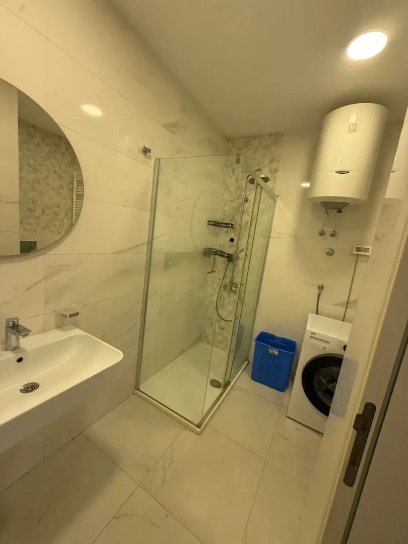 Modern bathroom with a shower cabin, washbasin, washing machine, and water heater.