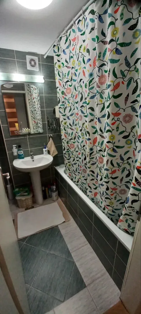 Kupatilo sa umivaonikom, ogledalom i kadom sa šarenom zavesom.