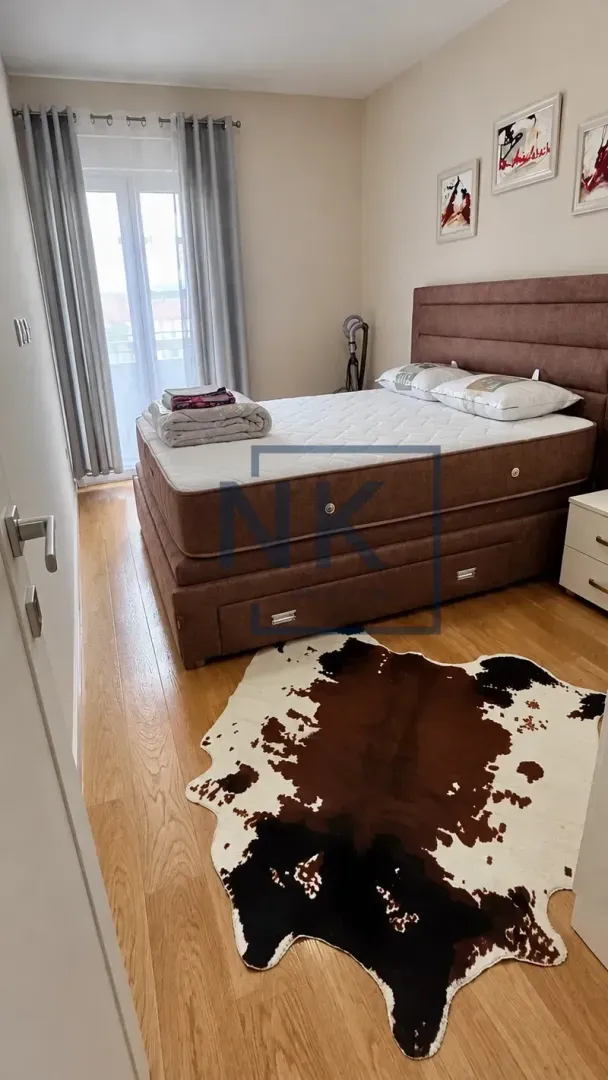 Namještena spavaća soba sa bračnim krevetom, drvenim podom i balkonskim vratima.
