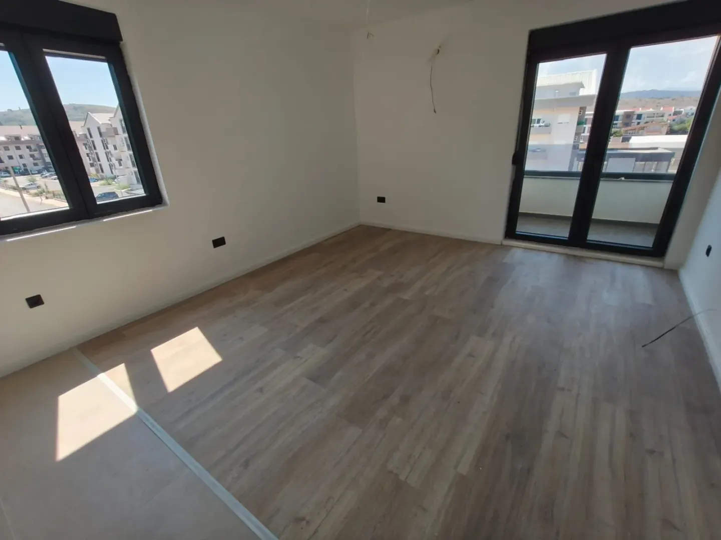 Empty unfurnished room with laminate flooring, white walls, and two windows.