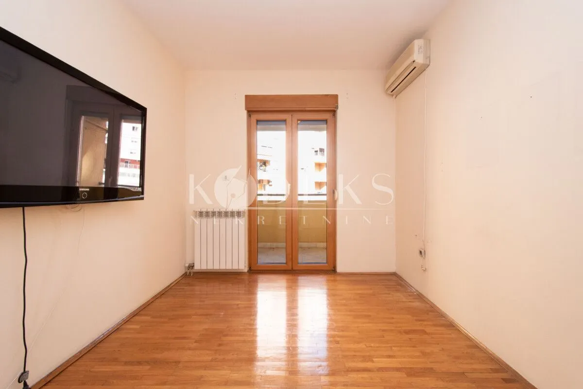 Empty living room with wooden flooring, wall-mounted TV, and balcony access.