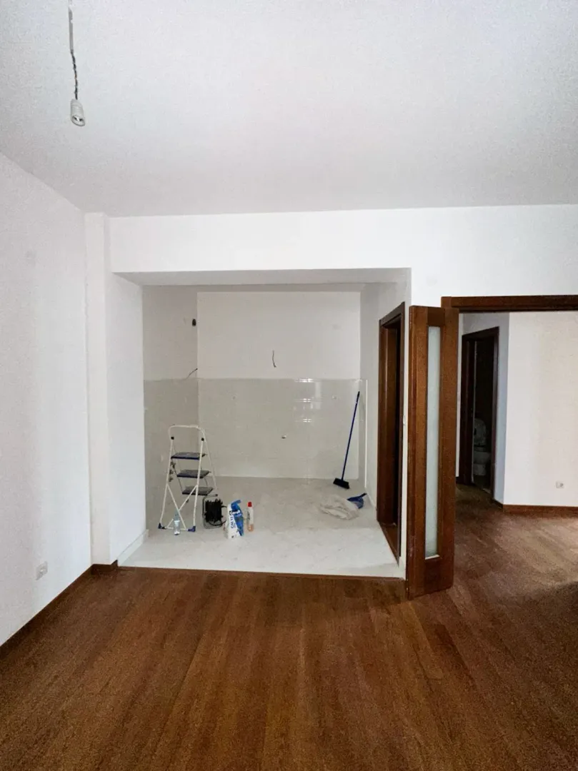 Prazna prostorija sa drvenim podom i pločicama u uglu pripremljenom za kuhinju.