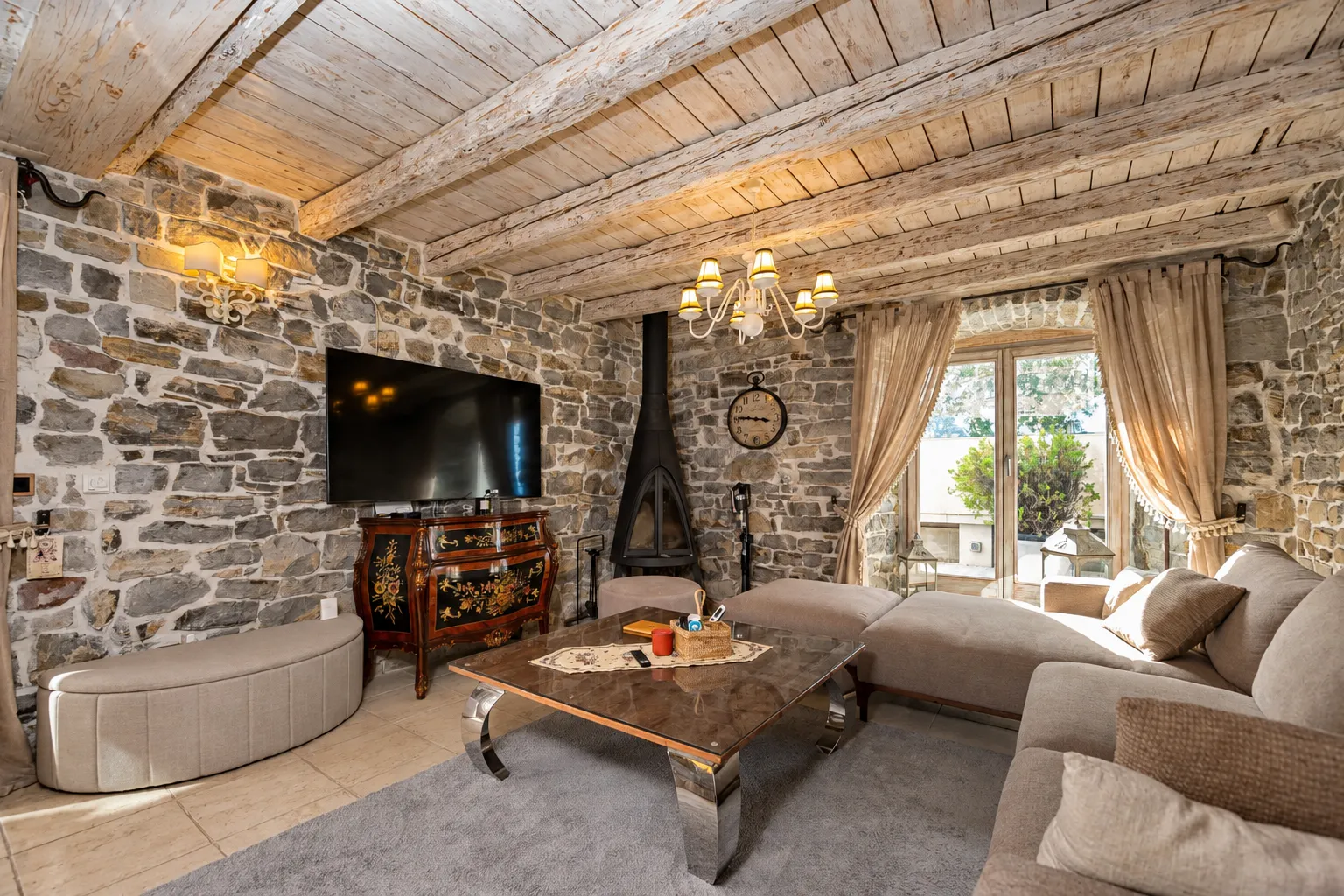 Living room with stone walls, wooden ceiling beams, and a fireplace.