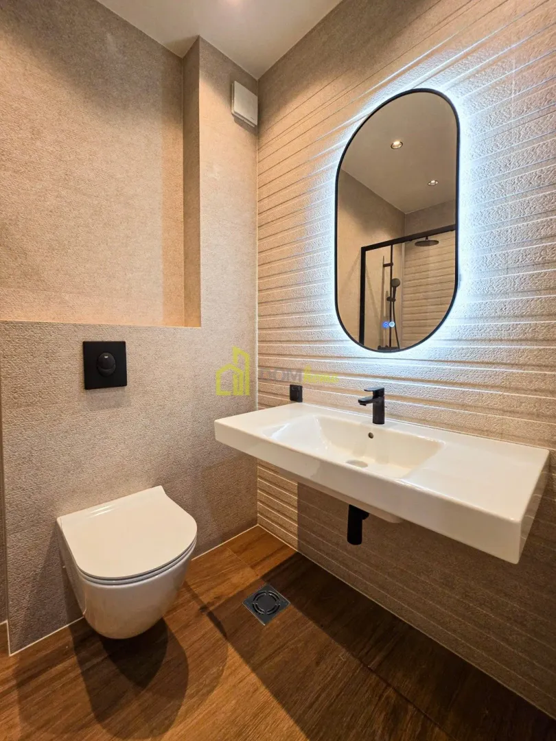 Modernly equipped bathroom with a washbasin, toilet, and backlit mirror.