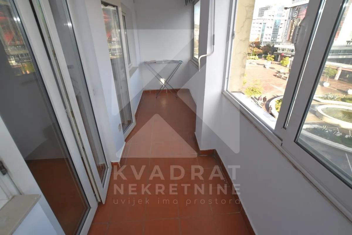 Zastakljeni balkon sa keramičkim pločicama i pogledom na grad.