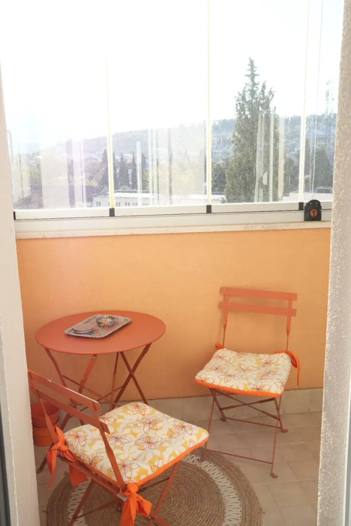 Enclosed balcony with seating furniture and a view of greenery.
