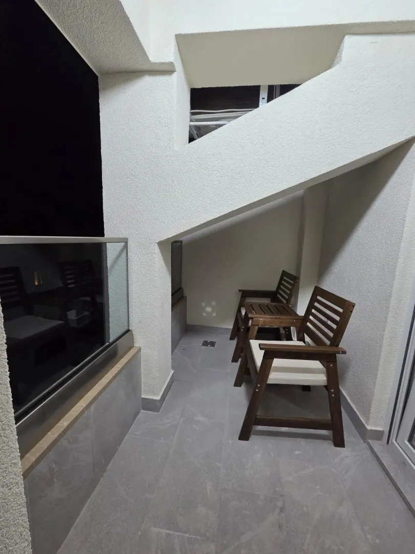 Natkriveni balkon sa drvenim stolicama i staklenom ogradom.