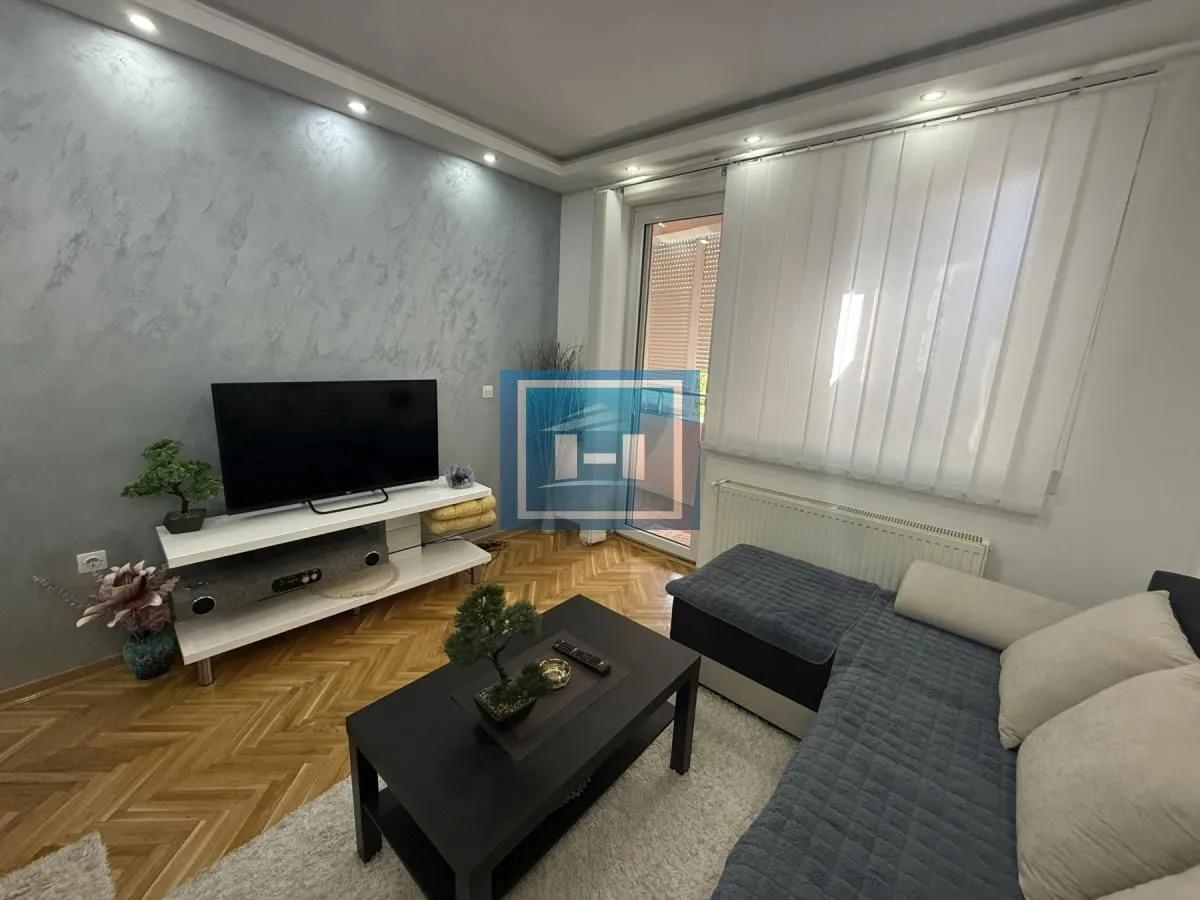 Dnevna soba sa ugaonom garniturom, televizorom i izlazom na terasu.